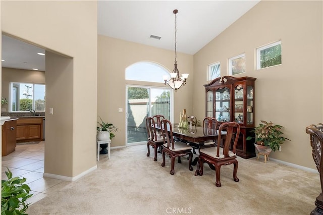 dining area with a notable chandelier, light colored carpet, high vaulted ceiling, and a healthy amount of sunlight