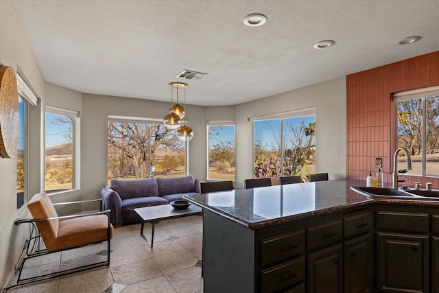 kitchen featuring decorative light fixtures, sink, dark stone countertops, light tile patterned floors, and a textured ceiling