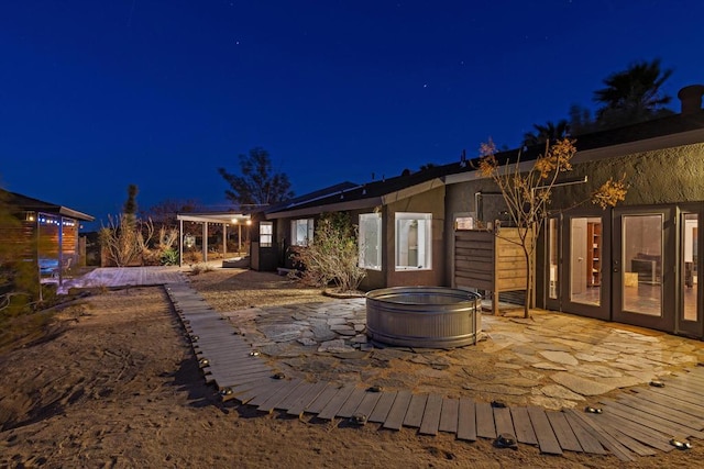 back house at night featuring a hot tub and a patio