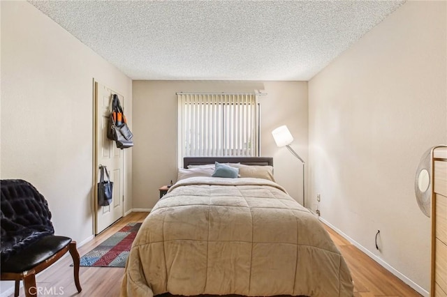 bedroom with a textured ceiling, wood finished floors, and baseboards