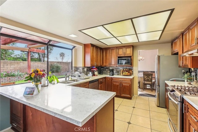 kitchen featuring under cabinet range hood, a peninsula, a sink, appliances with stainless steel finishes, and tasteful backsplash