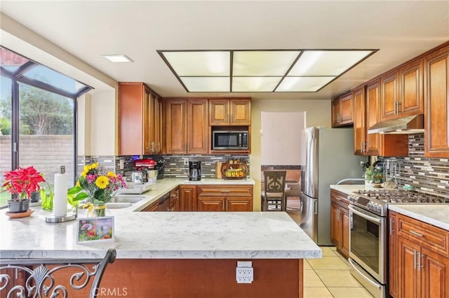 kitchen featuring tasteful backsplash, brown cabinetry, stainless steel appliances, under cabinet range hood, and light tile patterned flooring