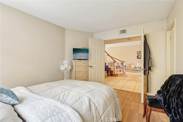 bedroom with light wood-type flooring, visible vents, and a textured ceiling