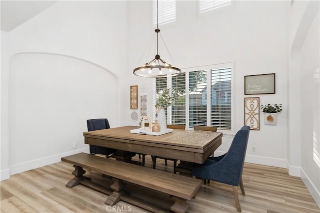 dining room with an inviting chandelier, light hardwood / wood-style floors, and a high ceiling