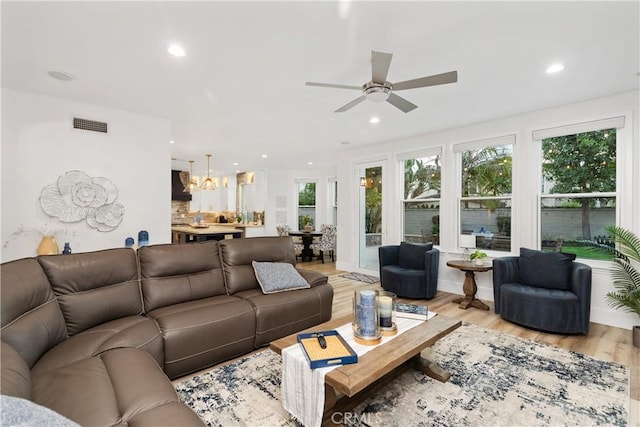 living room featuring ceiling fan with notable chandelier and light hardwood / wood-style floors