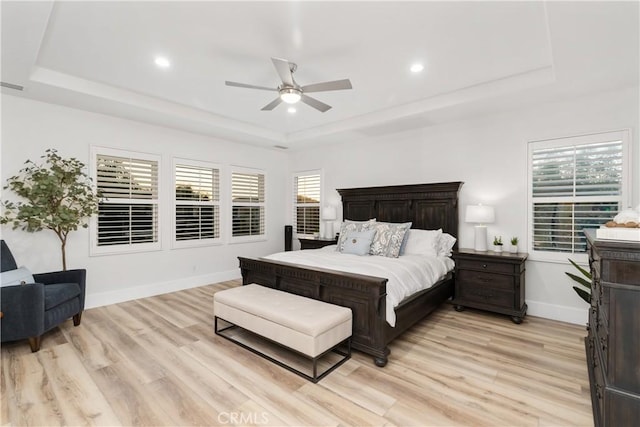 bedroom with a raised ceiling, ceiling fan, and light hardwood / wood-style floors