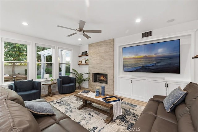 living room featuring a tiled fireplace, ceiling fan, and light hardwood / wood-style floors