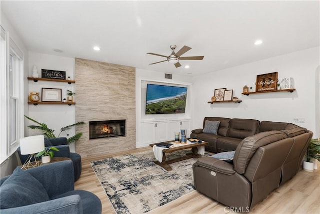 living room featuring a tile fireplace, ceiling fan, and light wood-type flooring