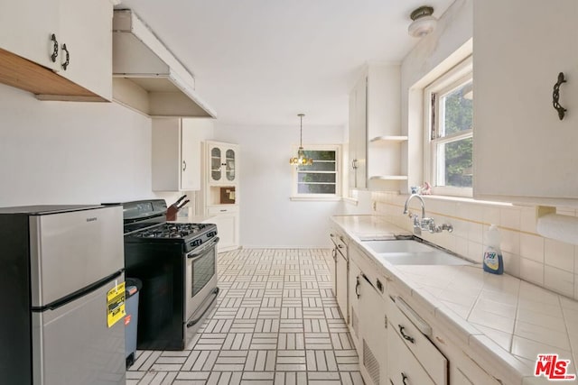 kitchen with appliances with stainless steel finishes, tile countertops, pendant lighting, ventilation hood, and sink