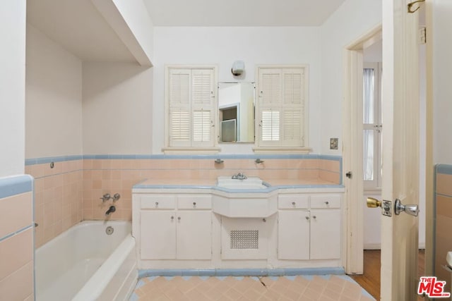 bathroom with vanity, tile walls, and a tub