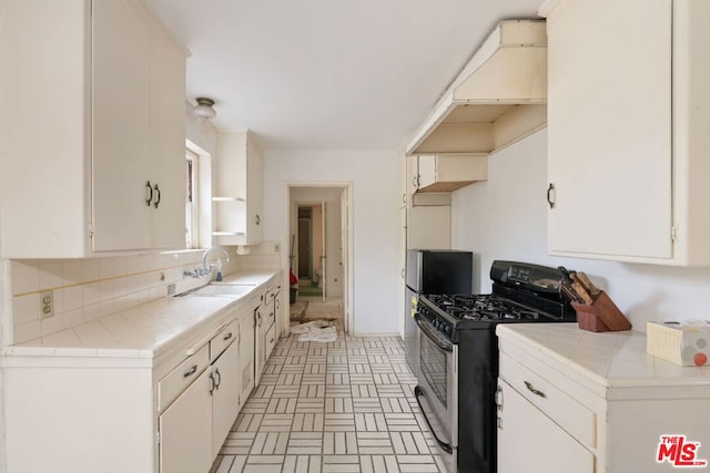 kitchen featuring tile counters, exhaust hood, gas stove, and white cabinets