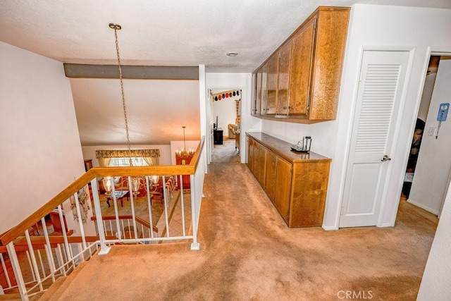 corridor featuring an inviting chandelier, baseboards, an upstairs landing, and light colored carpet