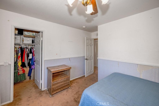 bedroom with light colored carpet, wainscoting, ceiling fan, a walk in closet, and a closet