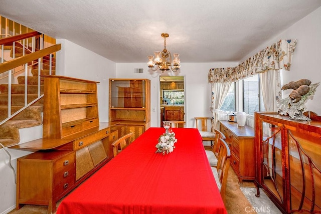 dining space with a textured ceiling, a notable chandelier, light carpet, visible vents, and stairs