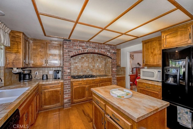 kitchen featuring light wood-style flooring, backsplash, tile counters, a center island, and black appliances