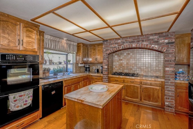 kitchen with a sink, a kitchen island, light wood-style floors, decorative backsplash, and black appliances