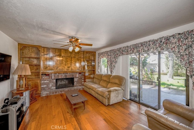 living area featuring built in shelves, a brick fireplace, a textured ceiling, and wood finished floors