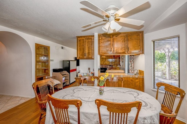 dining space with arched walkways, light wood-style floors, ceiling fan, a textured ceiling, and baseboards