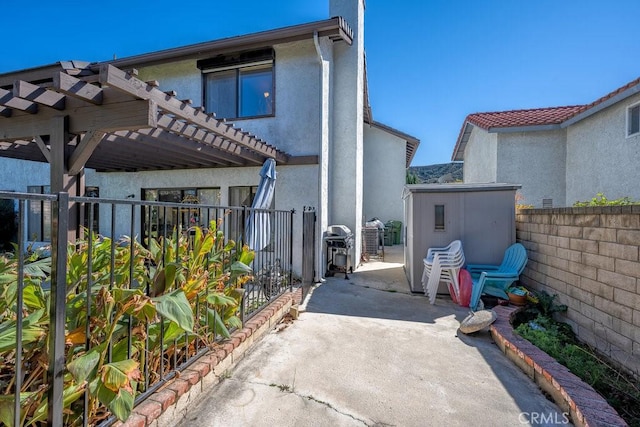 view of side of home with a patio, a storage unit, stucco siding, a pergola, and a fenced backyard