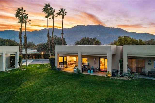 back house at dusk with a patio, a mountain view, and a yard