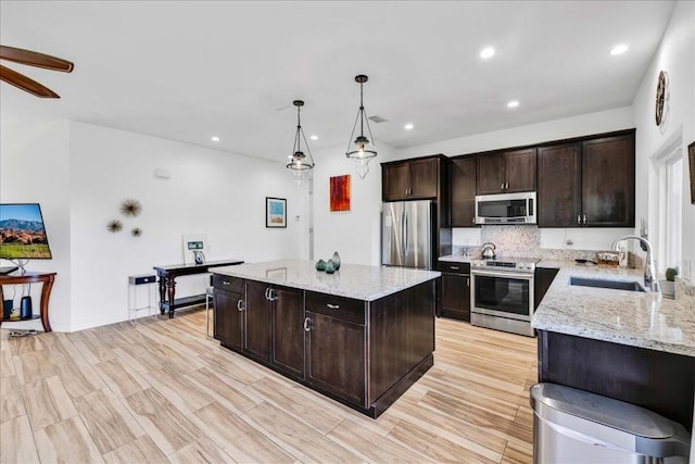 kitchen with sink, appliances with stainless steel finishes, hanging light fixtures, light stone counters, and a kitchen island