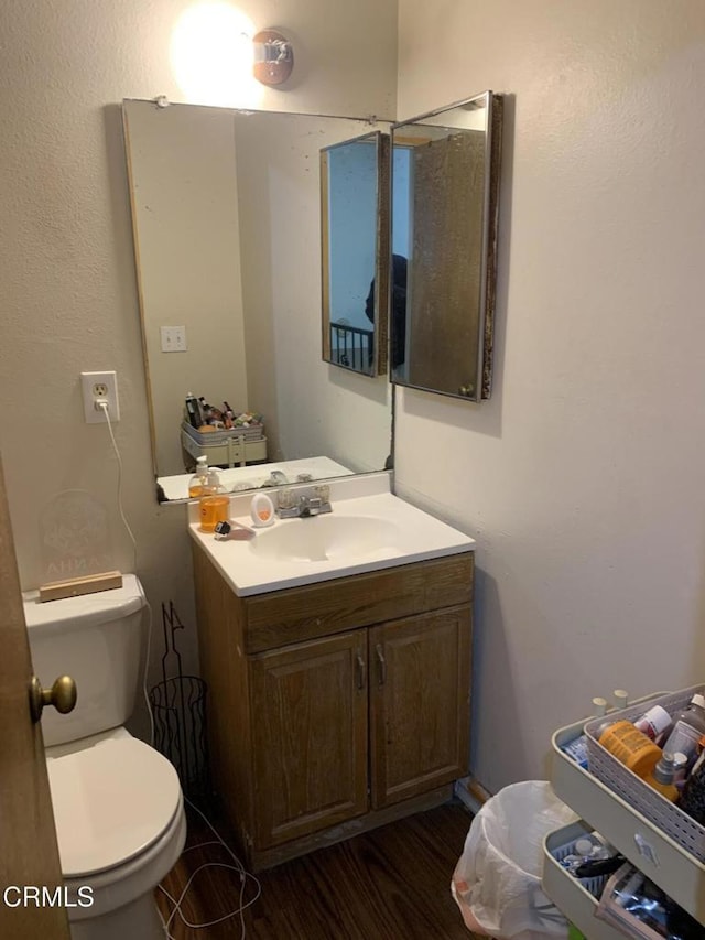 half bathroom featuring toilet, wood finished floors, and vanity