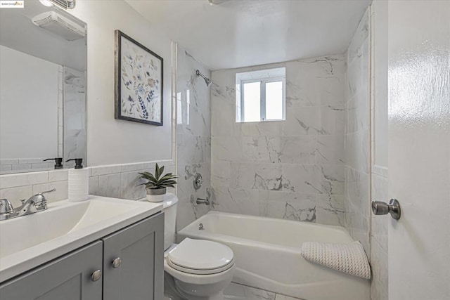 full bathroom with tiled shower / bath, vanity, toilet, and tile walls