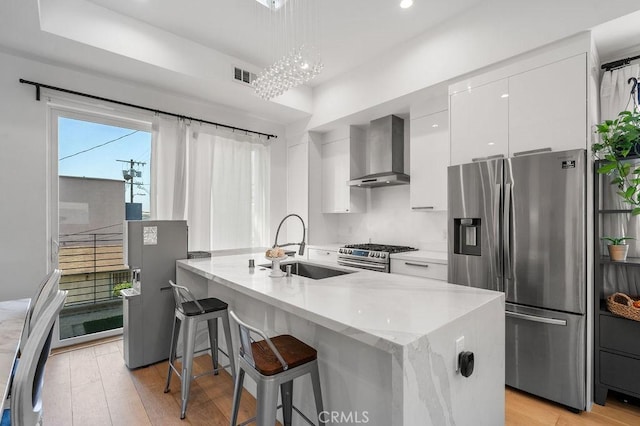 kitchen with visible vents, wall chimney range hood, appliances with stainless steel finishes, white cabinetry, and modern cabinets