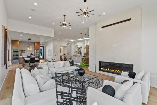 living room featuring a large fireplace, beverage cooler, a chandelier, and light hardwood / wood-style flooring