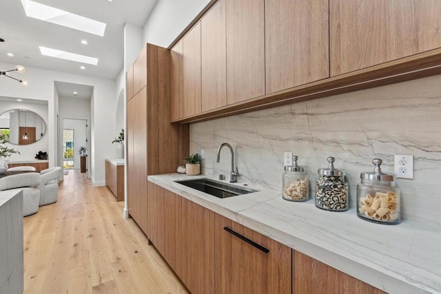 kitchen with sink, light hardwood / wood-style flooring, decorative backsplash, and a skylight