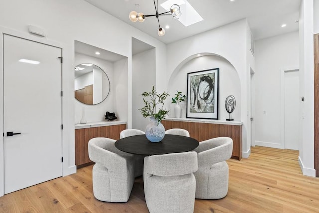 dining area featuring an inviting chandelier, light wood-type flooring, and a skylight