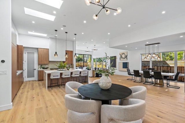 dining area featuring an inviting chandelier, a skylight, plenty of natural light, and light wood-type flooring