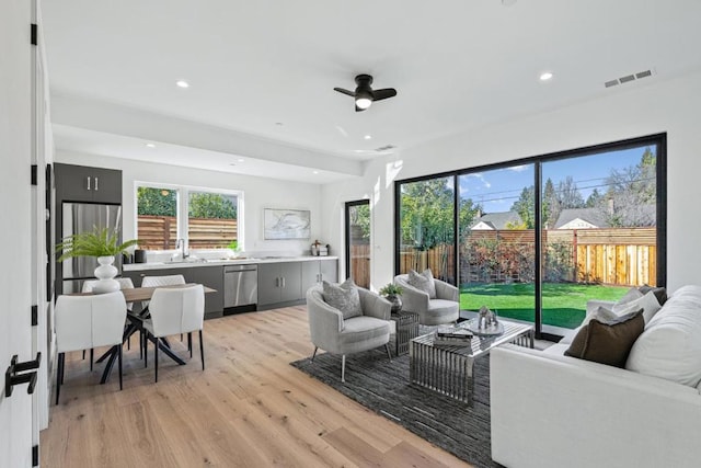 living room with ceiling fan, plenty of natural light, sink, and light wood-type flooring