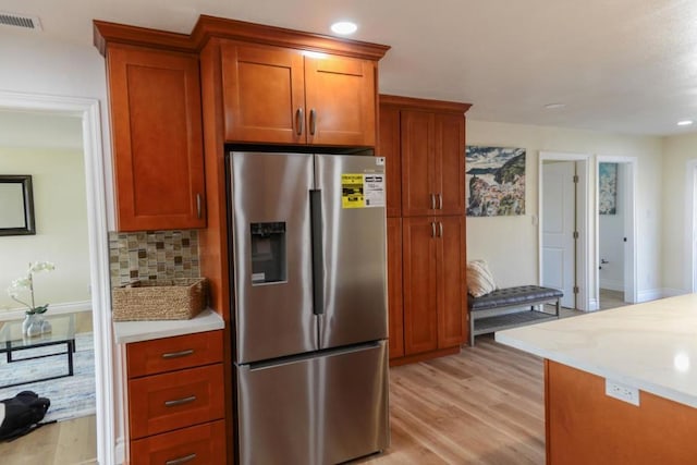 kitchen with light stone counters, stainless steel fridge, light hardwood / wood-style floors, and decorative backsplash