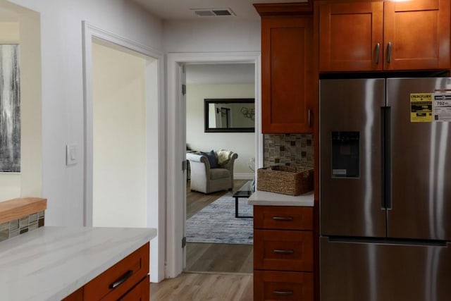 kitchen featuring light stone counters, stainless steel fridge with ice dispenser, decorative backsplash, and light hardwood / wood-style flooring