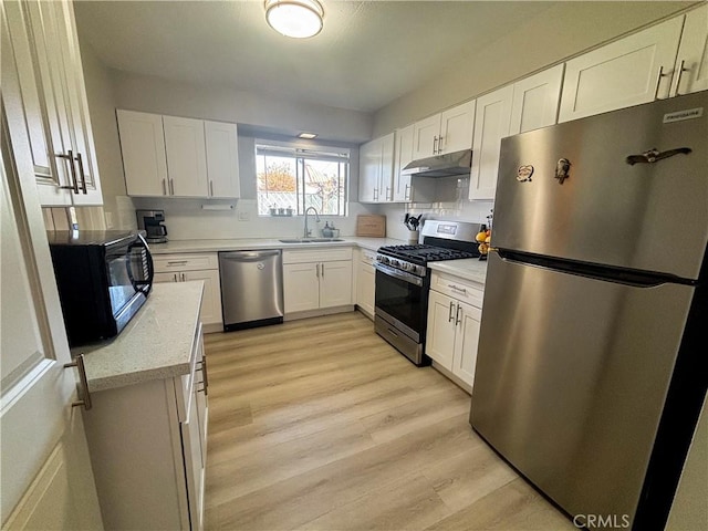 kitchen with under cabinet range hood, a sink, light wood-style floors, white cabinets, and appliances with stainless steel finishes