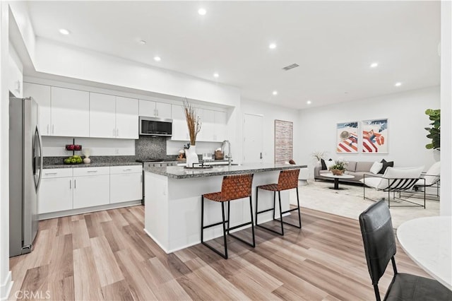 kitchen featuring appliances with stainless steel finishes, white cabinetry, a breakfast bar area, a kitchen island with sink, and light hardwood / wood-style flooring