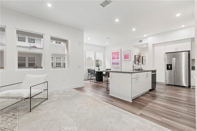 kitchen with a breakfast bar, white cabinetry, light hardwood / wood-style floors, stainless steel appliances, and a center island with sink