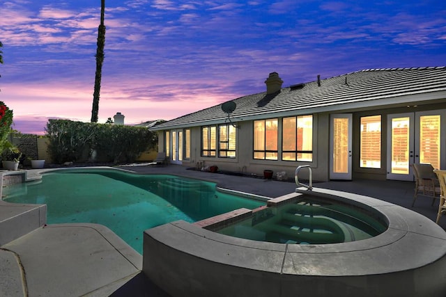 pool at dusk with a patio area and an in ground hot tub