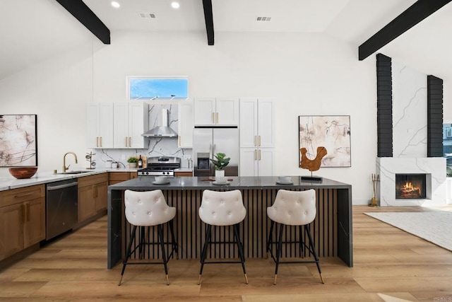 kitchen with wall chimney exhaust hood, a kitchen bar, sink, appliances with stainless steel finishes, and white cabinets