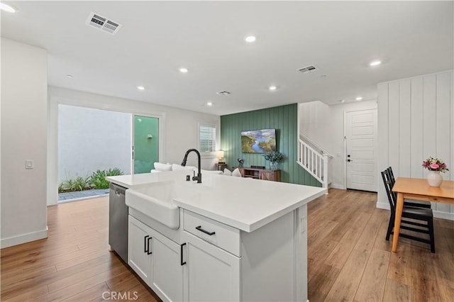 kitchen with light countertops, visible vents, a kitchen island with sink, a sink, and white cabinetry