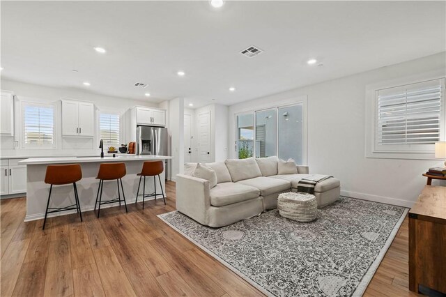 living area with light wood-type flooring, visible vents, baseboards, and recessed lighting