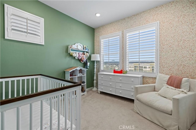 bedroom with light carpet, a nursery area, and wallpapered walls