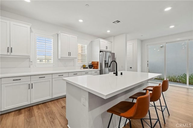 kitchen featuring white cabinets, light countertops, stainless steel refrigerator with ice dispenser, an island with sink, and a kitchen bar