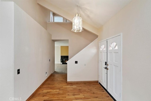 foyer entrance featuring an inviting chandelier, lofted ceiling, and light hardwood / wood-style flooring