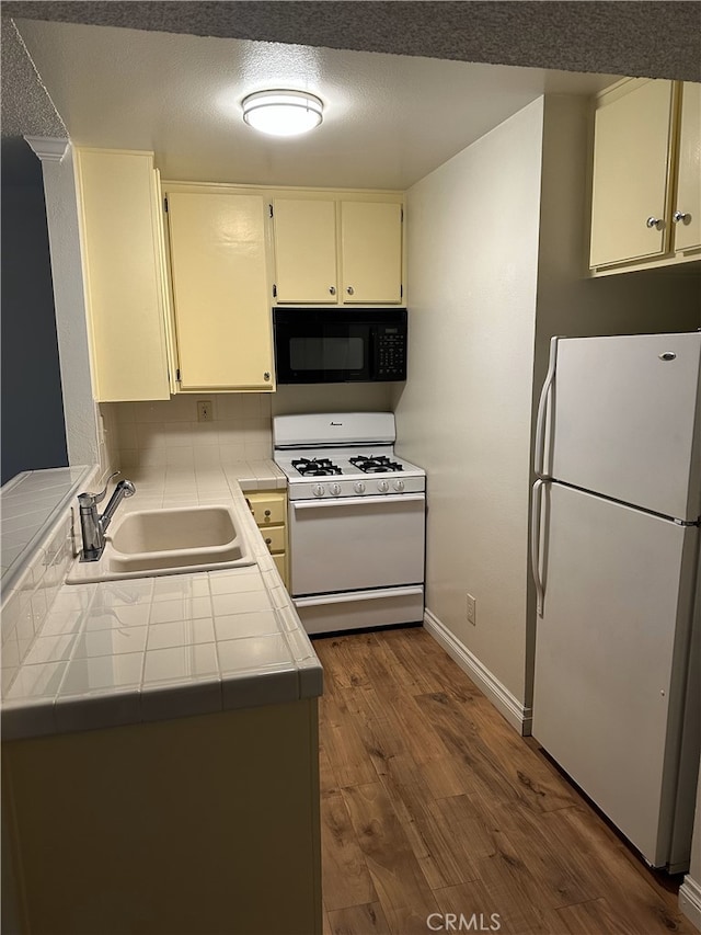 kitchen with dark wood-type flooring, sink, tile countertops, kitchen peninsula, and white appliances