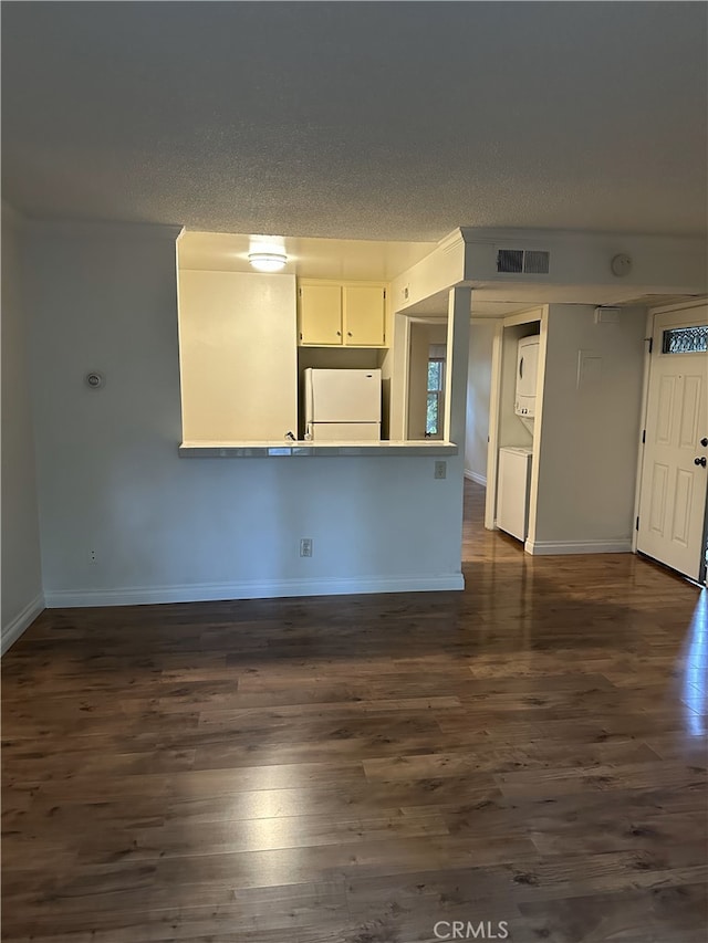 unfurnished living room featuring dark hardwood / wood-style floors, a textured ceiling, and stacked washing maching and dryer