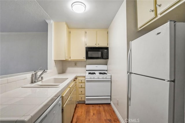 kitchen with sink, tile counters, white appliances, light hardwood / wood-style floors, and cream cabinetry