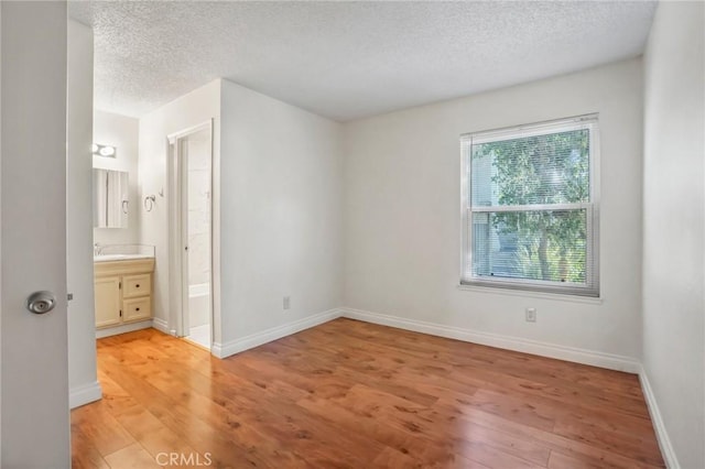 unfurnished bedroom with ensuite bath, a textured ceiling, and light hardwood / wood-style flooring