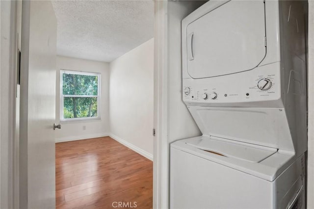 laundry room featuring stacked washer and dryer, hardwood / wood-style floors, and a textured ceiling